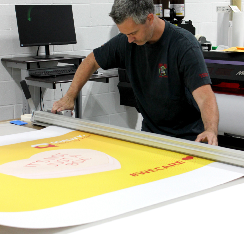 Employee inspecting a printed yellow banner on a large format print table in Columbus