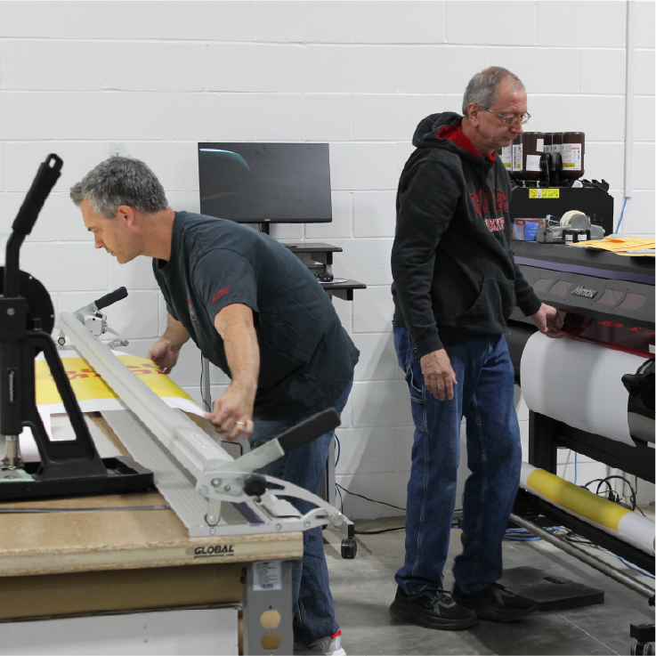 Technician feeding print media into a Mimaki wide format printer