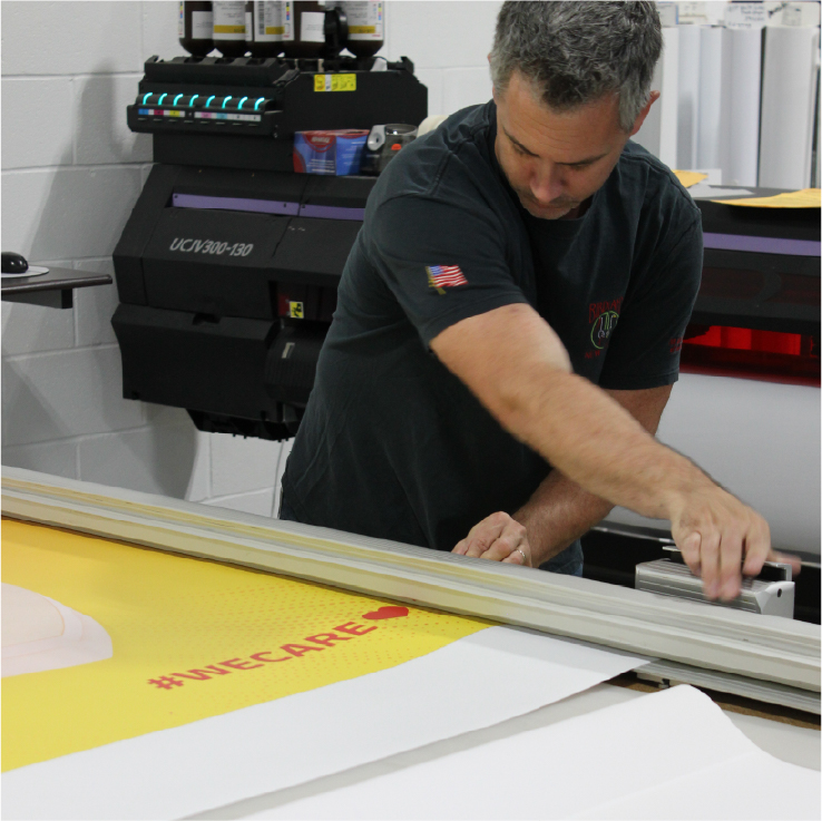 Two print shop employees operating a banner trimmer and wide format printer